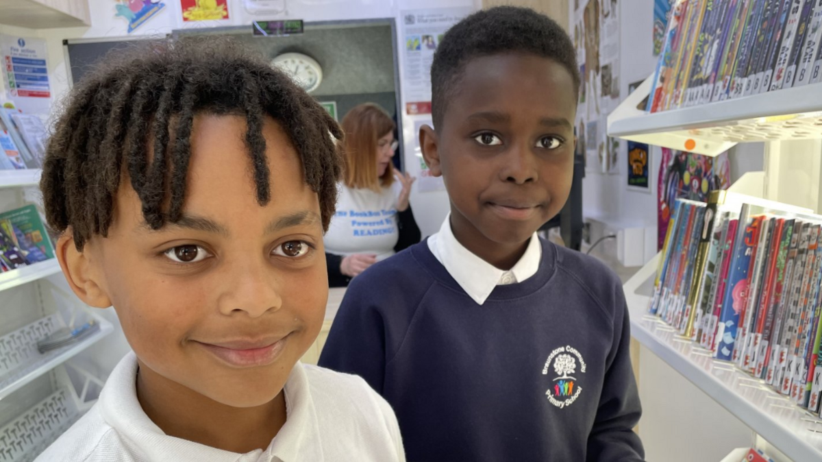 two boys stand inside the bus next to shelves of books smiling 