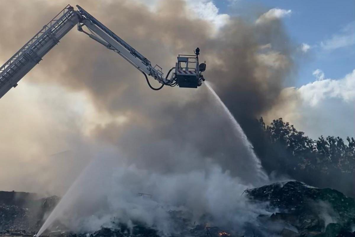 An aerial ladder platform hosing down a pile of smouldering waste