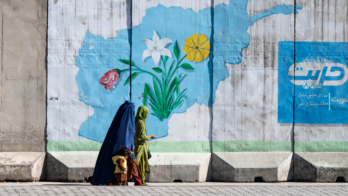 An Afghan burqa-clad woman walks past a wall mural with the map of Afghanistan, in Kabul on February 1, 2024. (Photo by Wakil KOHSAR / AFP) (Photo by WAKIL KOHSAR/AFP via Getty Images)
