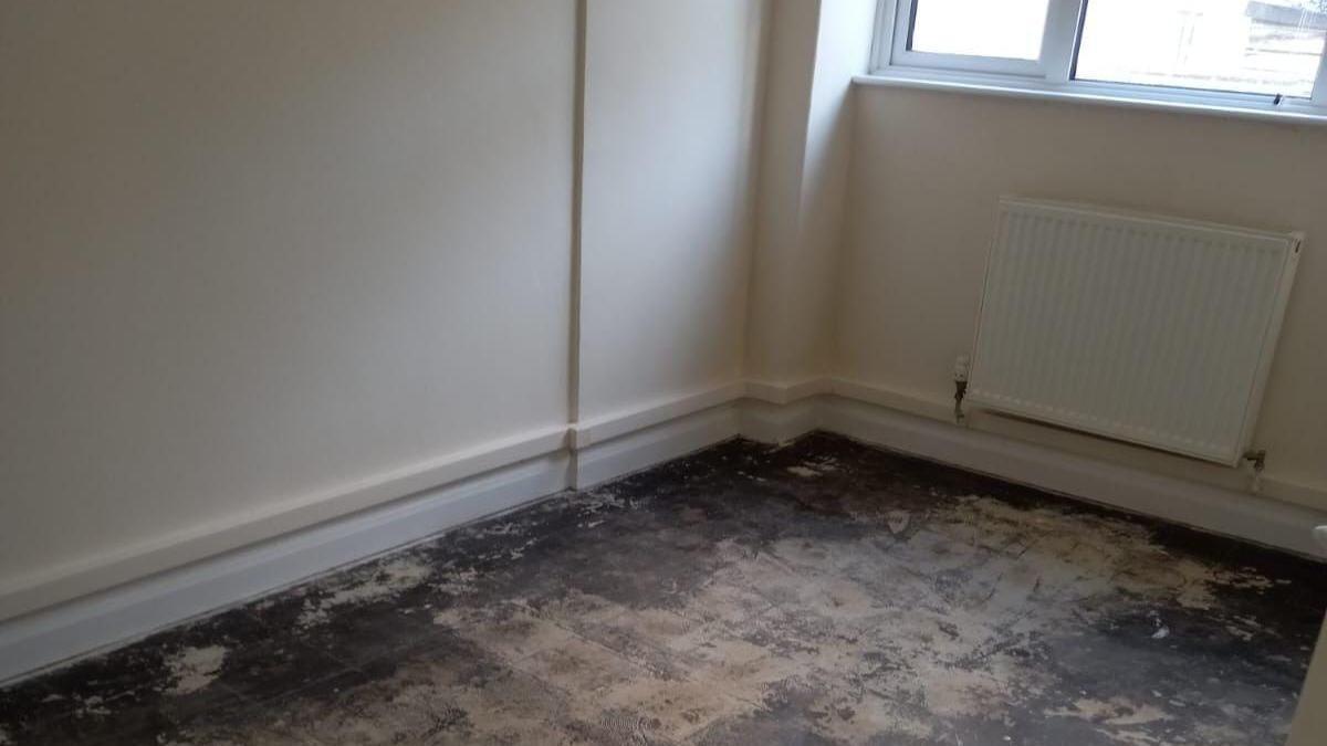 A small, empty room with heavily worn wooden floorboards, next to a radiator and double glazed window.