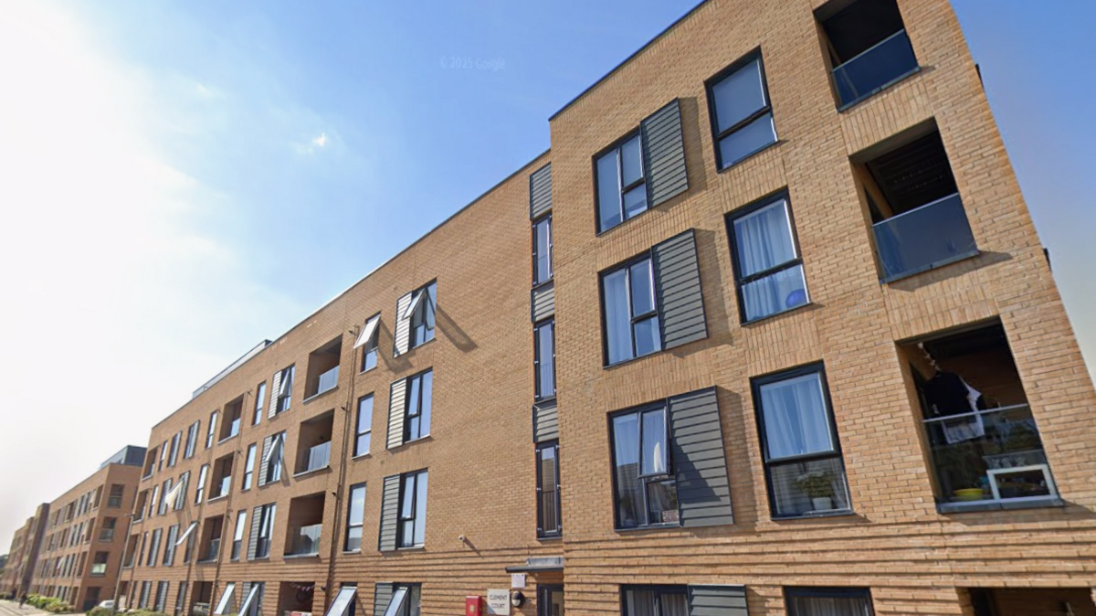 A block of flats - the building is three storeys high and has light brown bricks and dark windows.