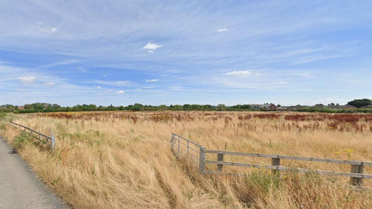 Grass fields and fences pictured against a background of a blue sky and clouds.