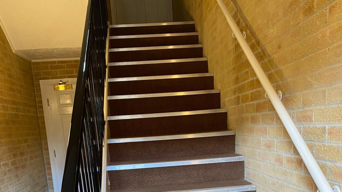 A staircase with brown carpet and a black bannister for support.