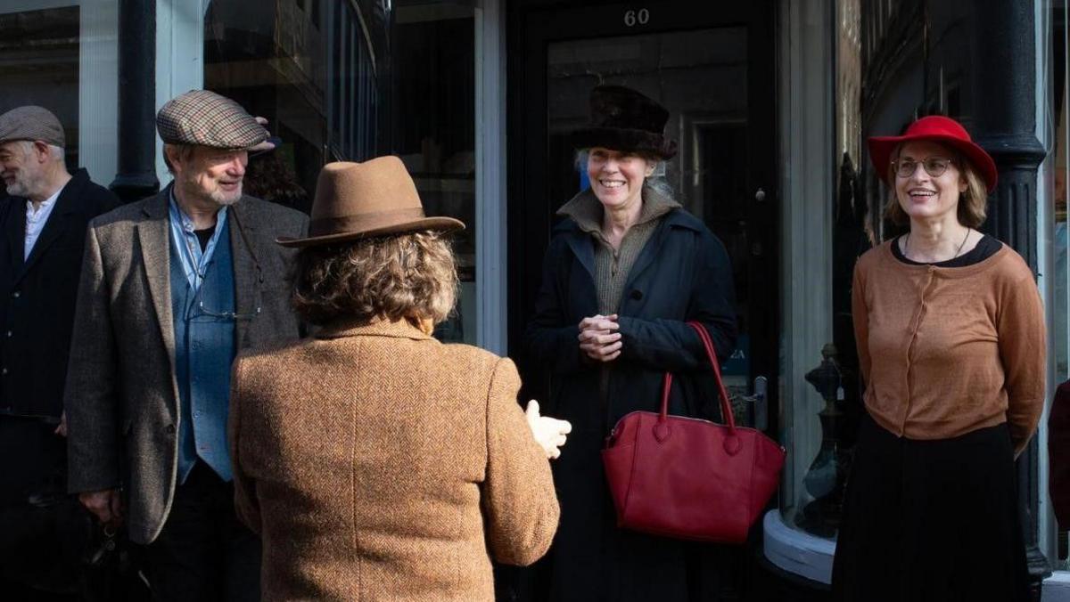 Four people in 1930s clothing chatting in a doorway 