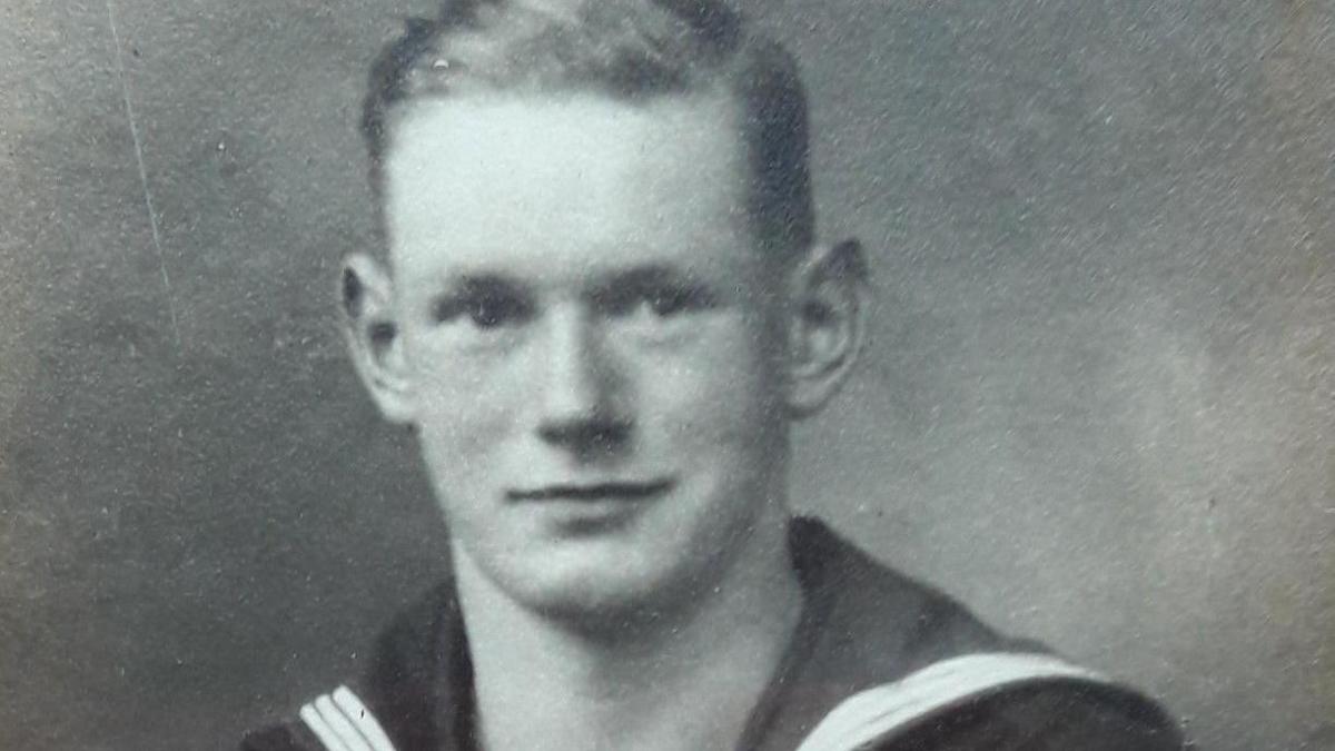 Bill Redston in a black and white image dressed in a Royal Navy uniform. He has short, dark hair with a side parting and is clean shaven.