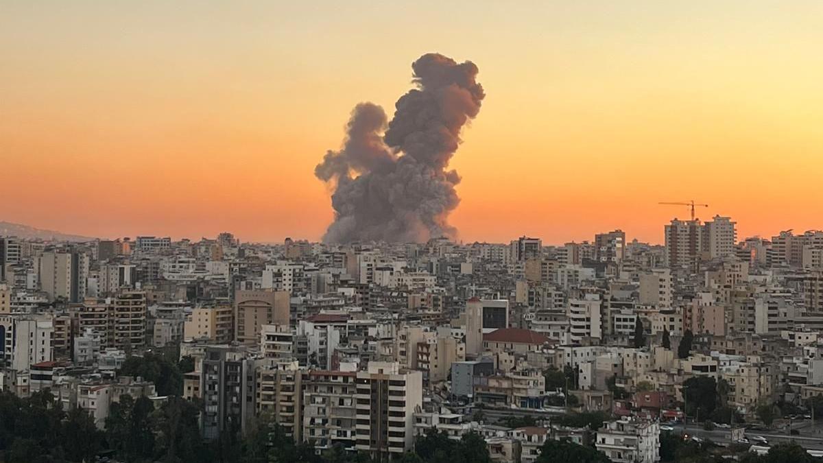 The skyline of Beirut, with a plume of smoke seen rising up on the horizon against a burnt orange skyline. 