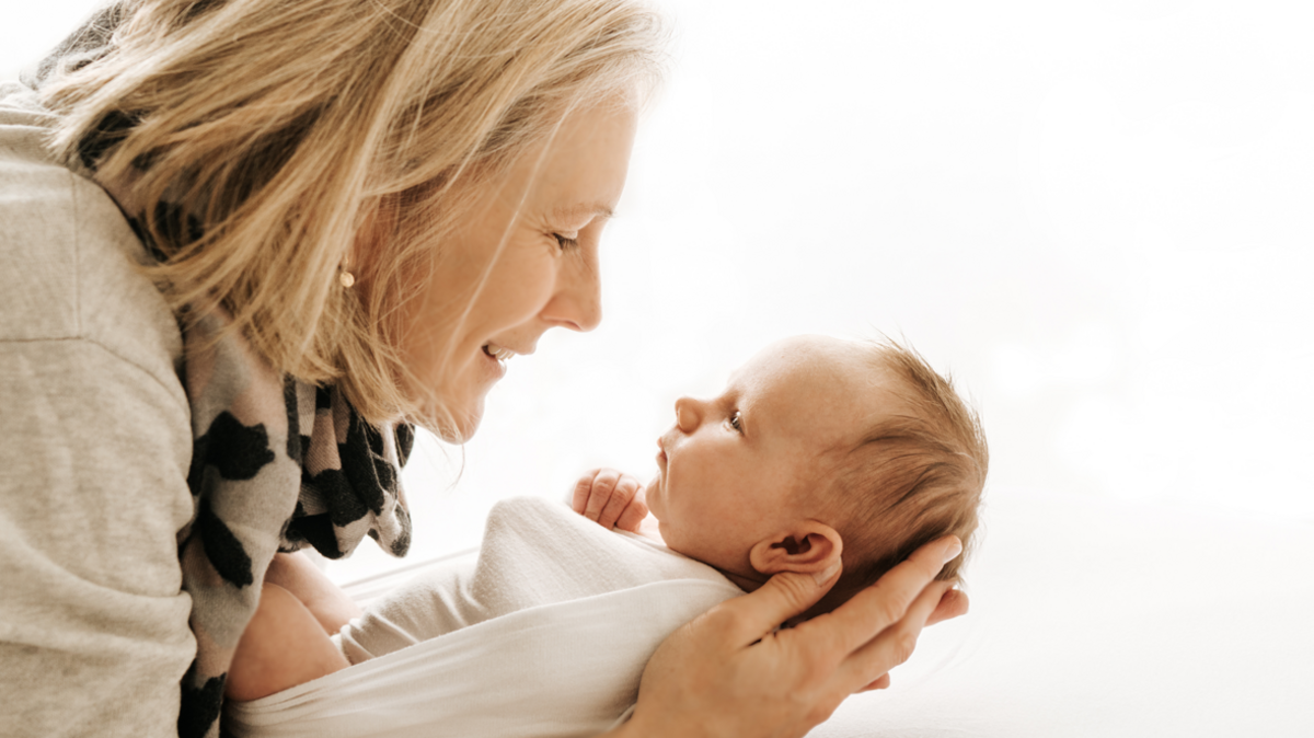 Sophie, who has a blonde bob and wears gold drop earrings with a grey jumper and a grey, pink and black scarf, cradles her new-born daughter Martha, who is dressed in swaddling clothes