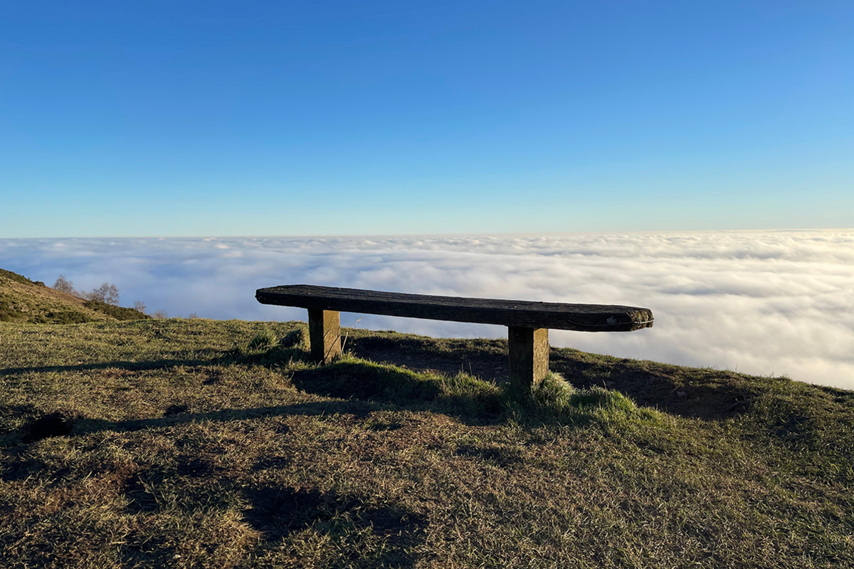 Malvern mist with a bench near the top of a hill and lots of cloudy white mist visible beyond.