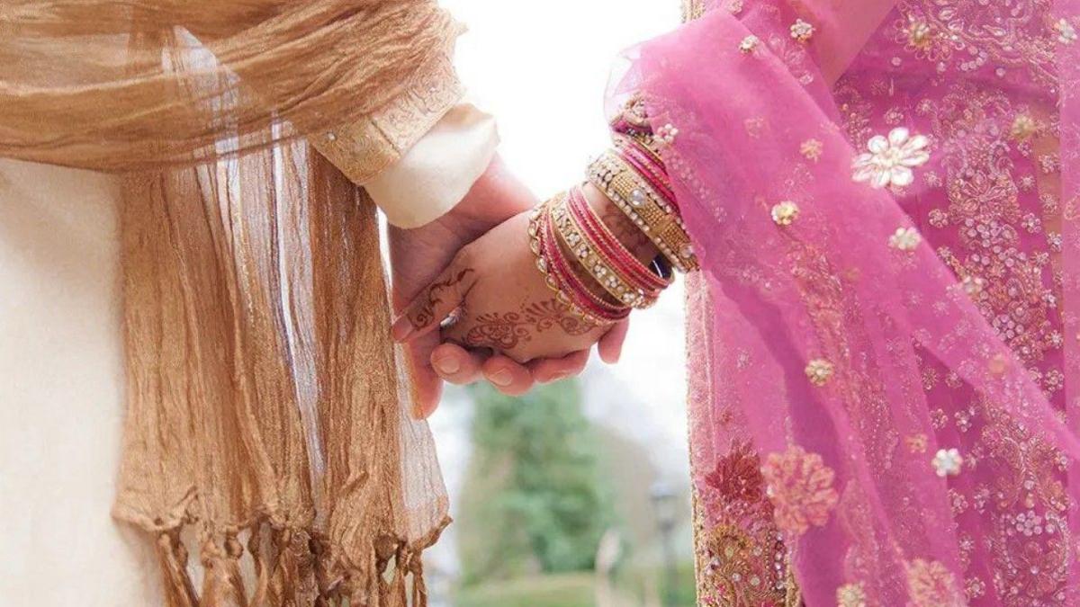 A man and a woman holding hands. The woman on the right is wearing a pink sari and the man on the left is wearing a traditional sherwani.