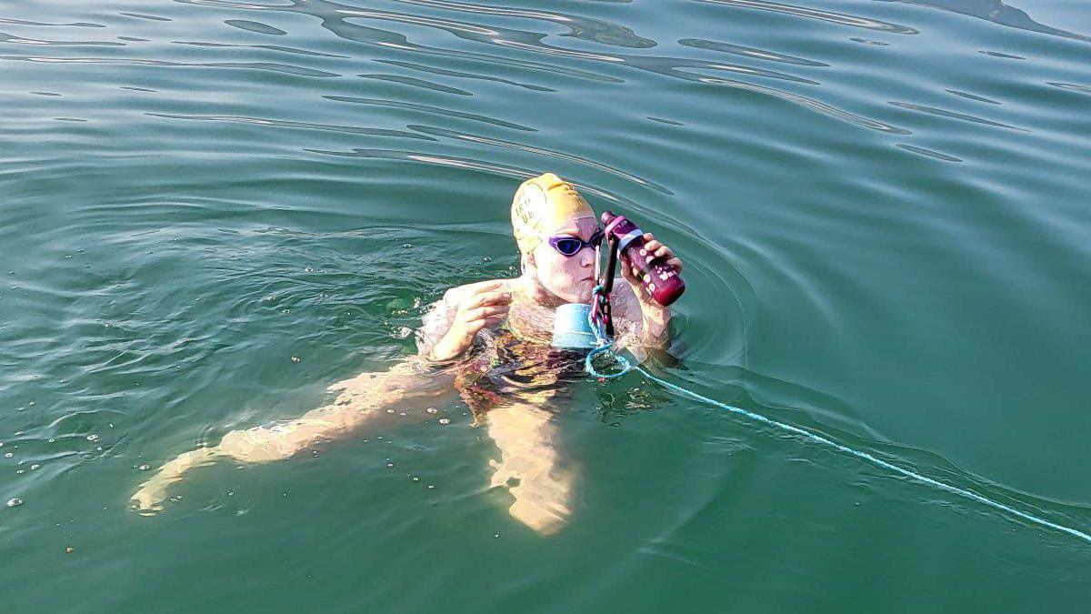 Food and drink on the end of a rope in a lake is held by a swimmer in a hat and goggles. 