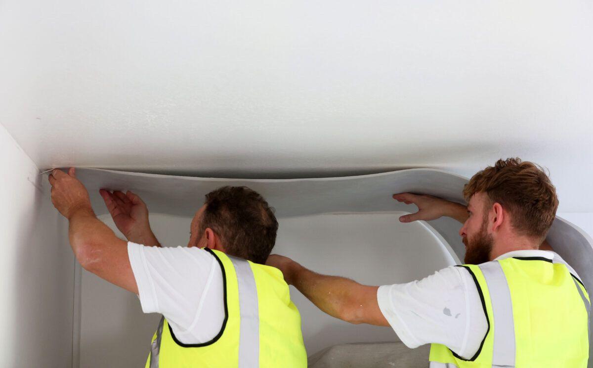 Two men paste electric wallpaper to a ceiling