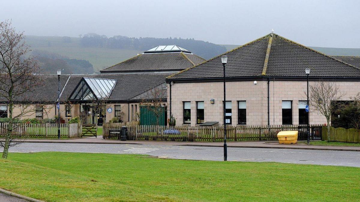 Laurencekirk Primary school building, behind a wooden fence, under a cloudy sky.