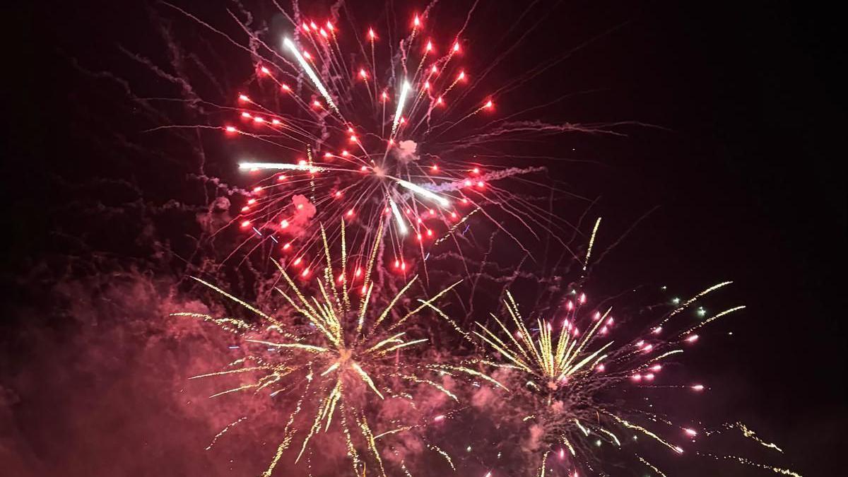 Three red and yellow fireworks exploding in the sky, spraying sparks and smoke outwards.