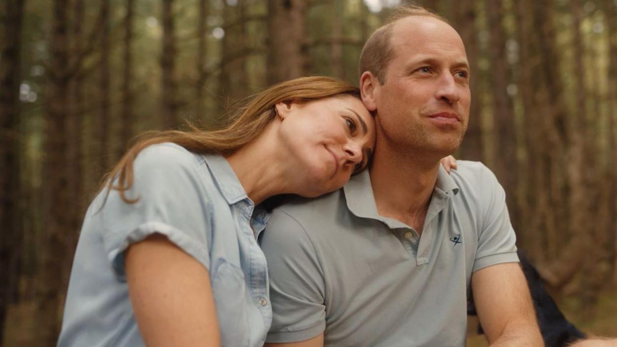 Catherine and William gaze into the distance while holding one another in a forest clearing Norfolk in the film which is filtered to appear sepia in tone.