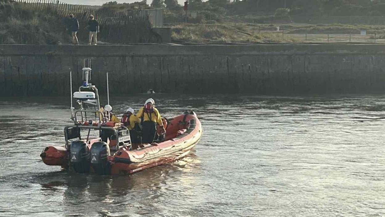 Three lifeboat crew members in a lifeboat in the River Blythe approaching the harbour wall.