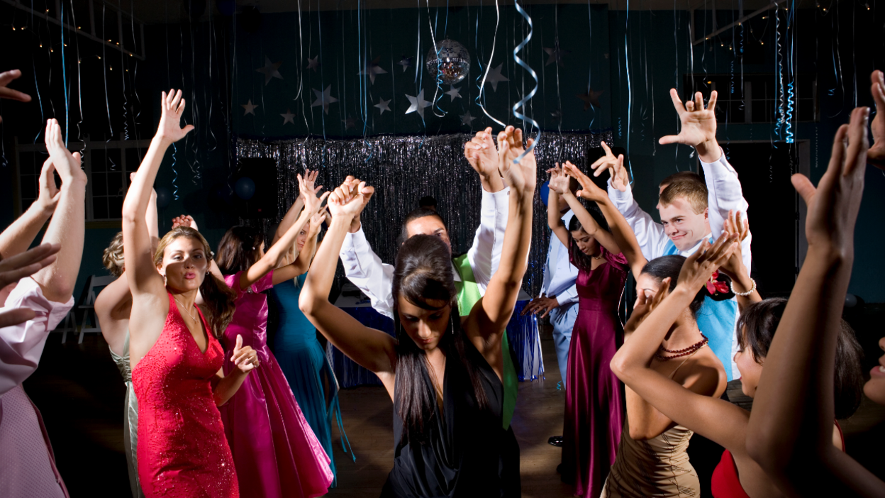 A stock image of teenagers dancing at a school prom. The girls wear different coloured dresses and the boys wear shirts and waistcoats