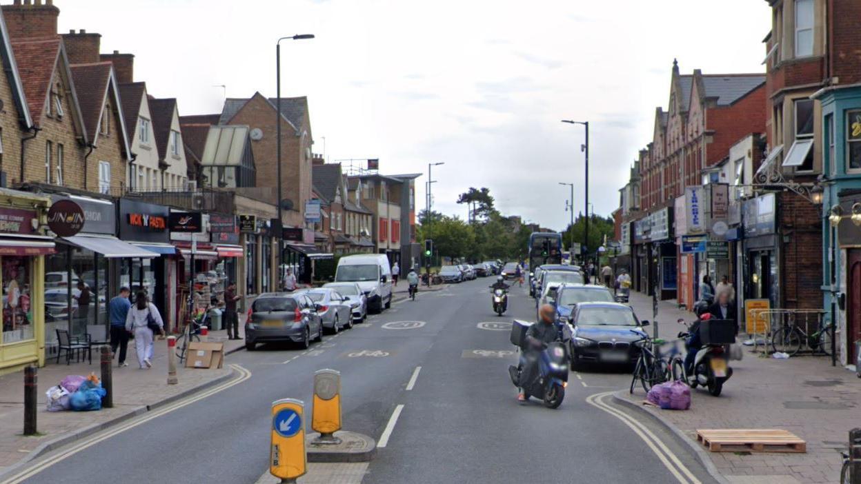 A street view image of Cowley Road. It is a busy thoroughfare with shops and restaurants on either side.