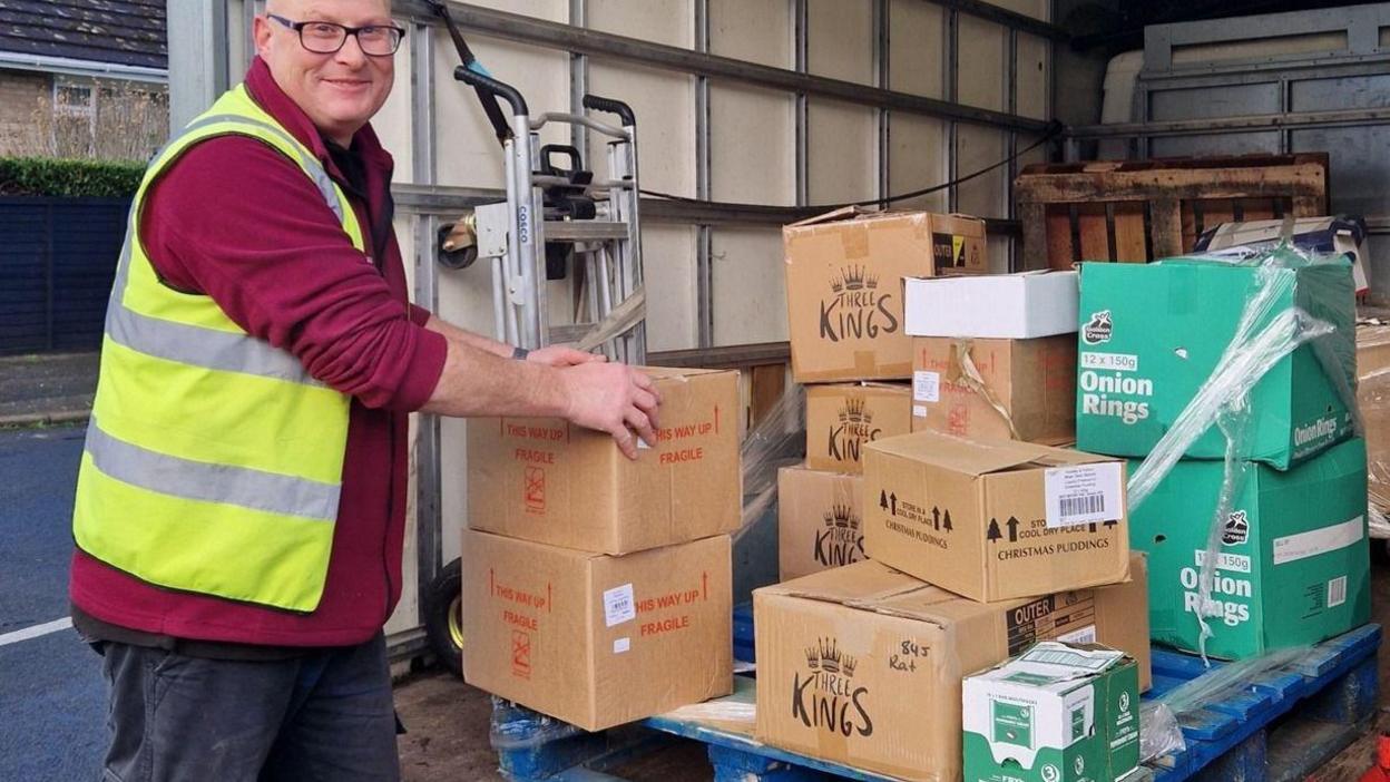 A man in a hi-vis jacket picking up boxes of food from a lorry.