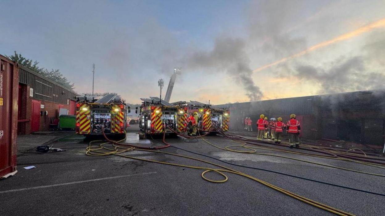 Three fire engines and firefighters at Tulketh Industrial Estate tackling a fire at commercial units. Smoke can be seen rising in the air.