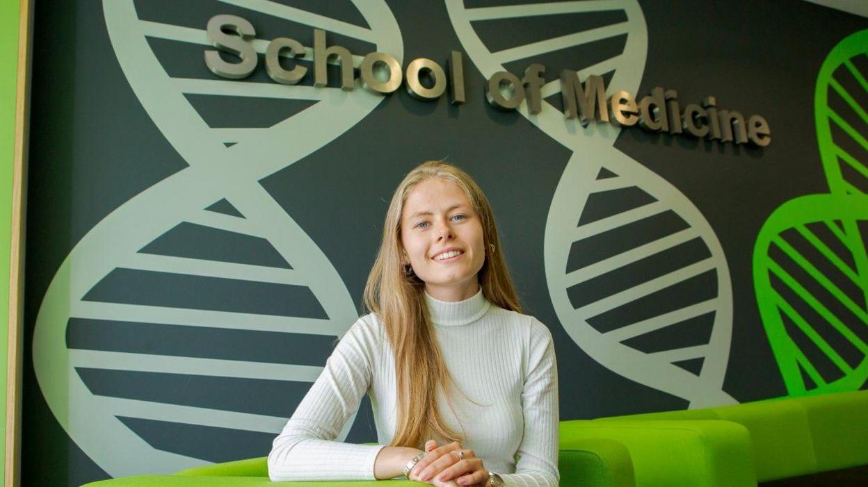 Laura Giles, who has long blonde hair, smiling at the camera and sitting on a green couch.