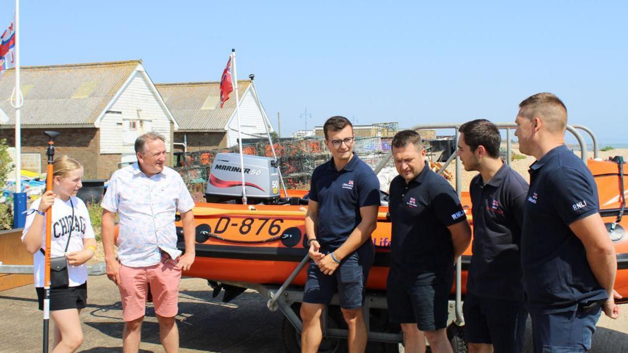 Steve and Alyssa stand on the left, smiling gratefully at their rescuers at a lifeboat station