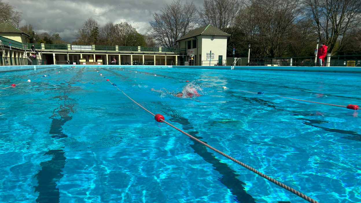 Peterborough Lido, with clear blue water and a swimmer splashing while moving along a lane in the pool