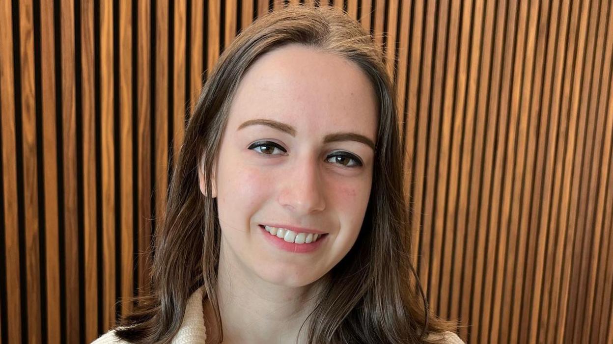 Megan Gilkes looking at the camera and smiling with a wood panelled wall behind her