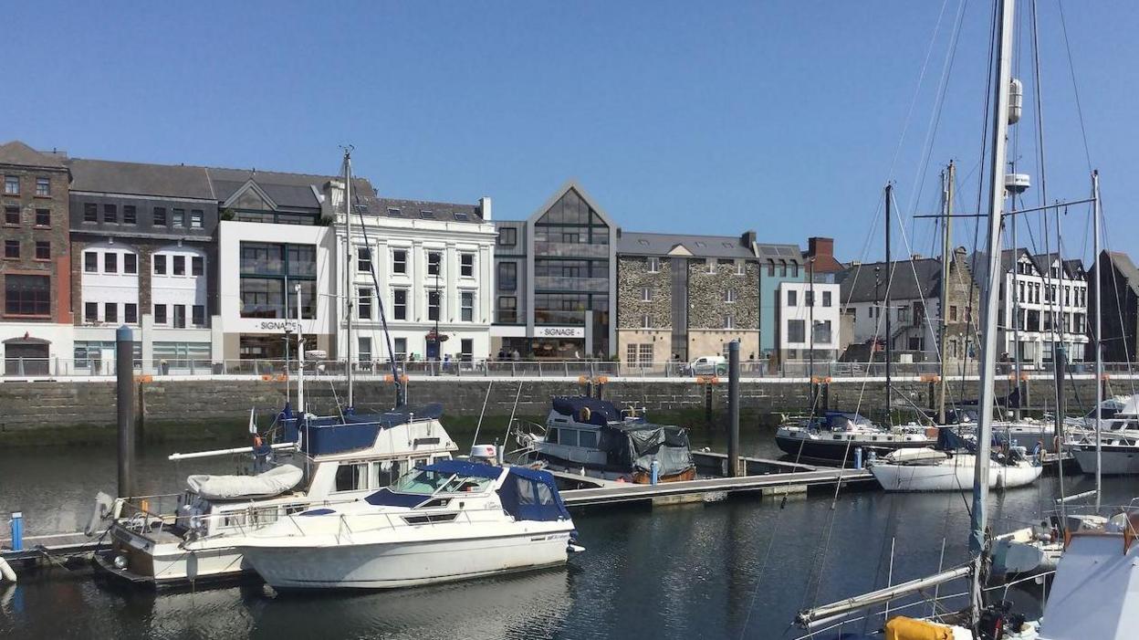 The view from across Douglas quay features a variety of modern and old buildings, including the former Newson's site which is stone, and a modern white building next to it.