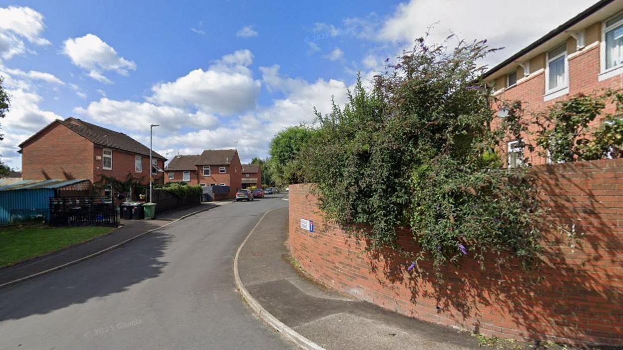 A brick wall with houses behind and a street sign reading Melville Gardens