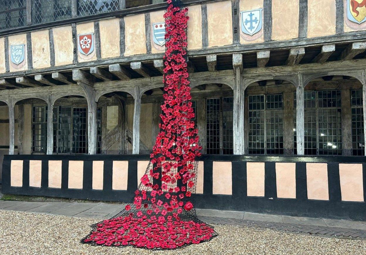 Dozens of ceramic poppies in a half-timbered medieval courtyard. They are hanging from the first floor via netting and some are on the ground.