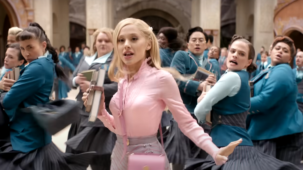 A still from the film shows Grande dancing, dressed in pink, with other students dressed in blue. All of them are holding school books. On the far right of the image is Tegan Browne-Winter.