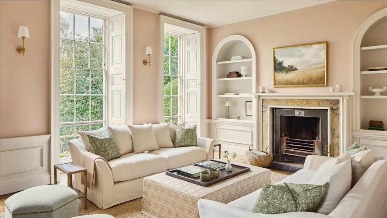 A beautiful taupe and white coloured living room with white sofas and sage green cushions. The room has large georgian looking windows.