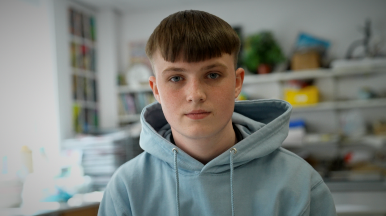 Kian is a Year 11 pupil. He is looking into camera, has short brown hair and is wearing a blue hoodie. 