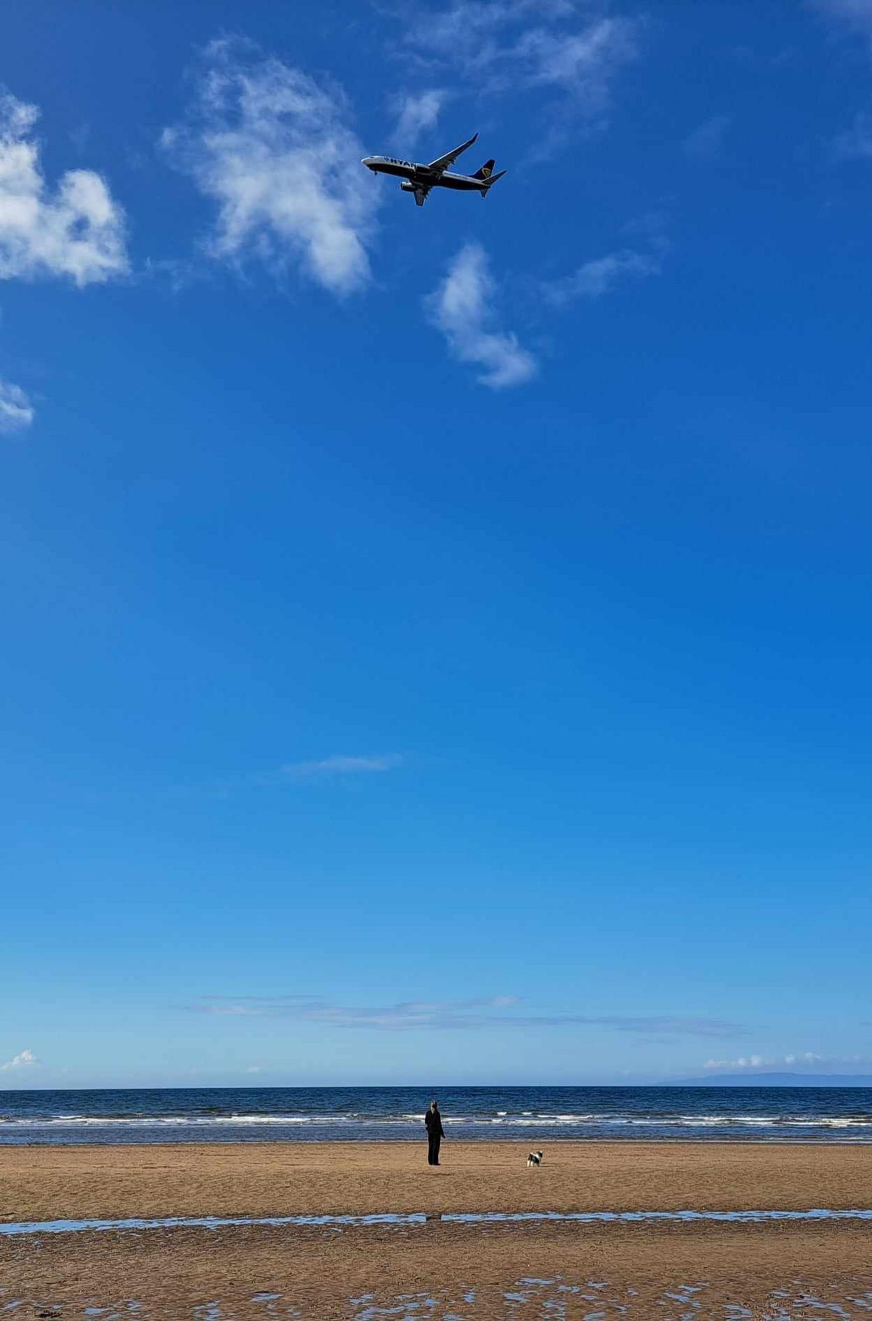 Shadow of a woman and a dog standing on a beach as a plane fly's overhead