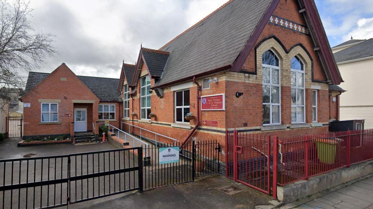 An older, Victorian-style red brick school building with short metal fences around it.