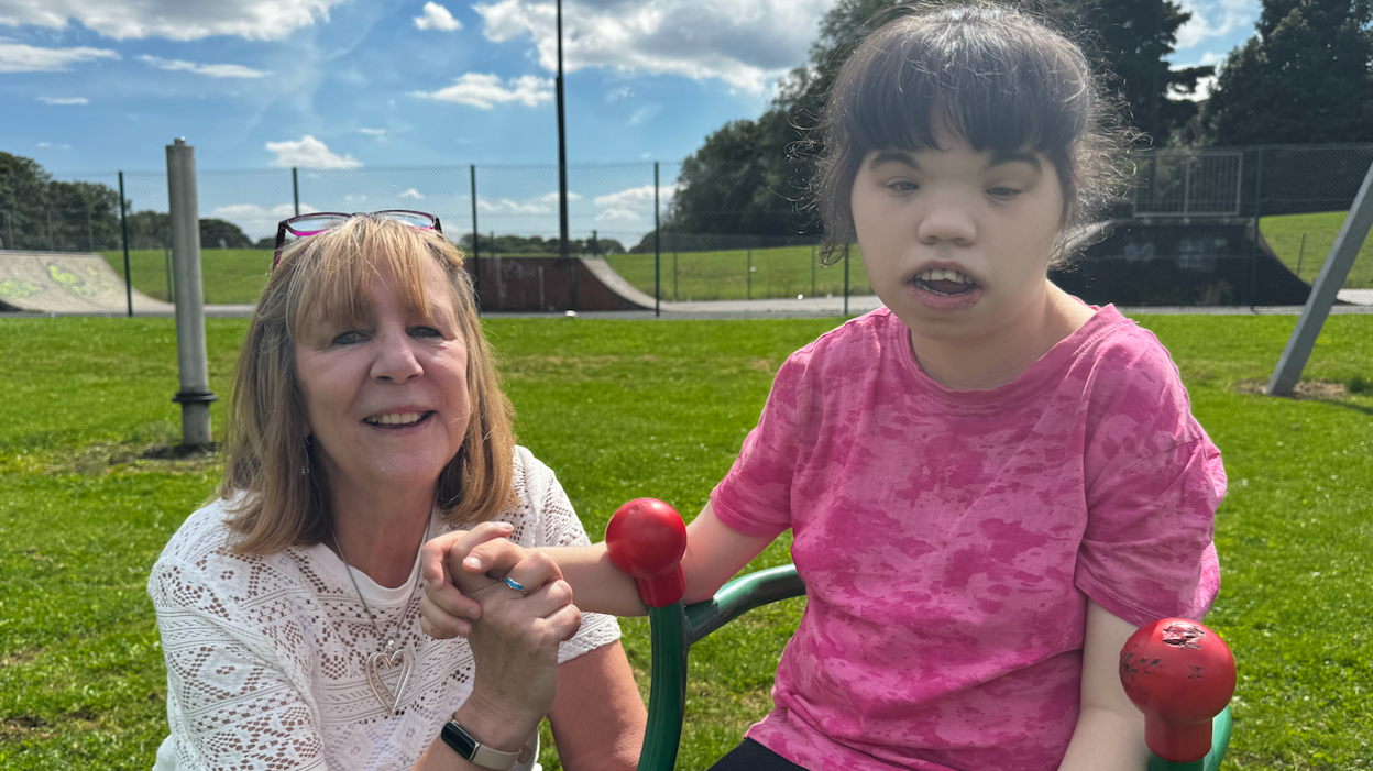 A woman sits with her daughter on playing equipment.