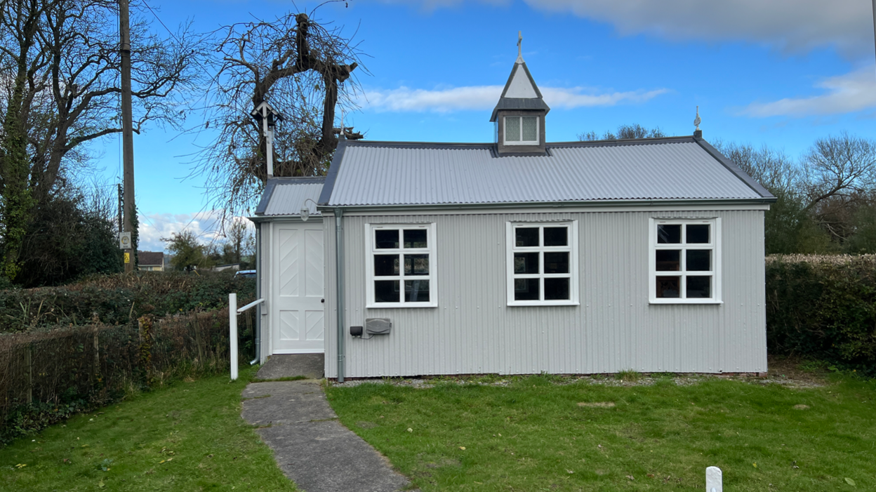 The tin church seen from the outside. There is a path leading up to the entrance. 