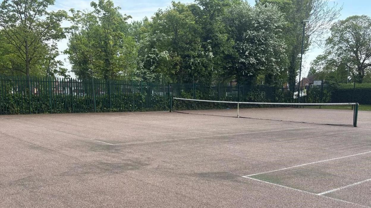 A tennis court which is grey with marks on it.