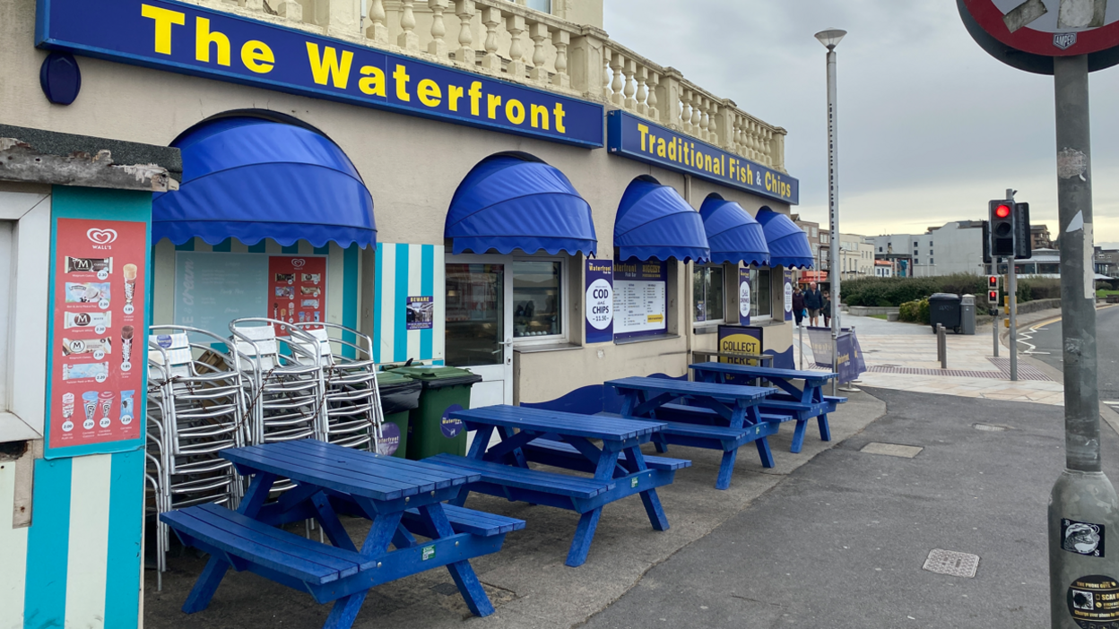 Four blue wooden benches outside the fish and chip shop by the seafront in Weston-super-Mare on an overcast day.