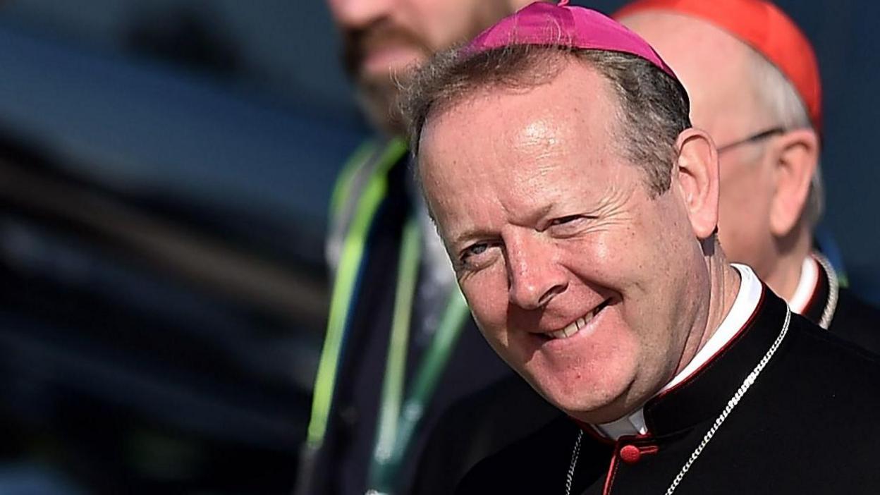 Archbishop Martin is smiling at the camera. He is wearing a pink zucchetto (Cardinal's cap) and black robes.