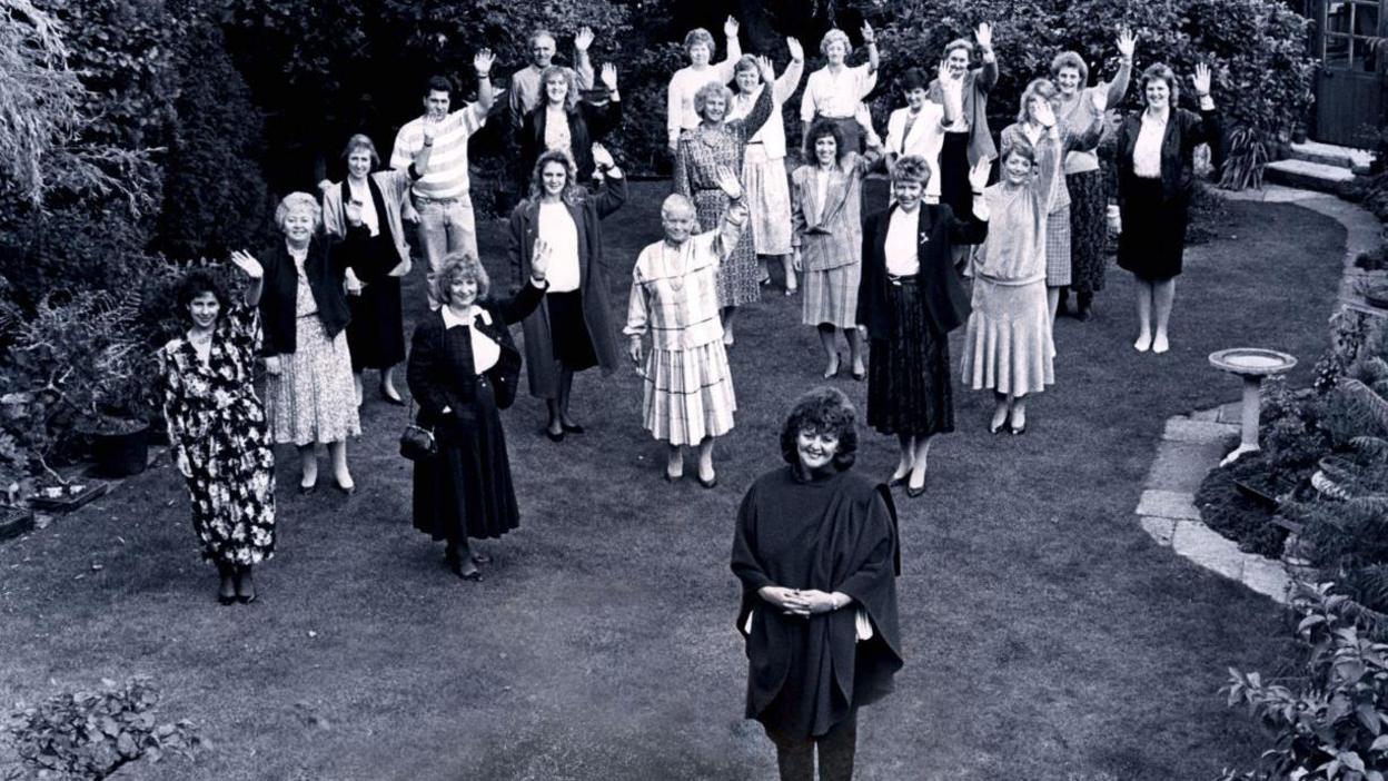 A black and white photo of Margaret Miles-Bramwell with Slimming World head office staff stood behind her in 1989 