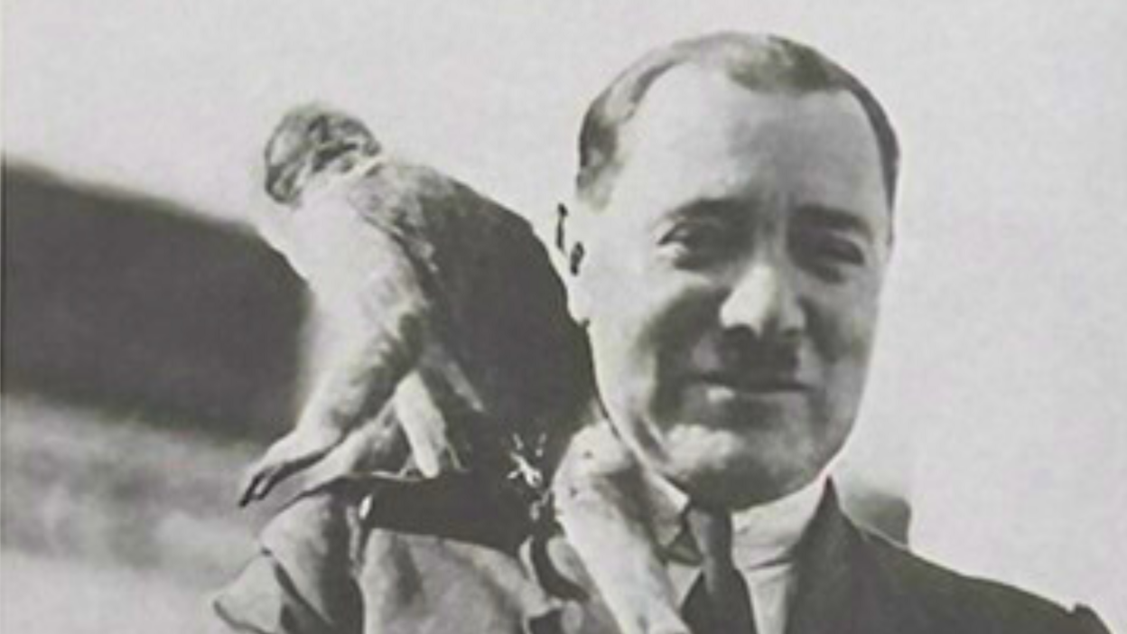 A black and white image of Captain Douglas Ann with a monkey on his left shoulder. Captain Ann is wearing a suit and tie.