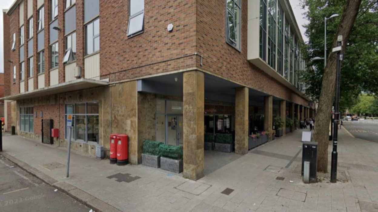 A brick building, with windows on each floor, and planters to the left and right of the corner entrance