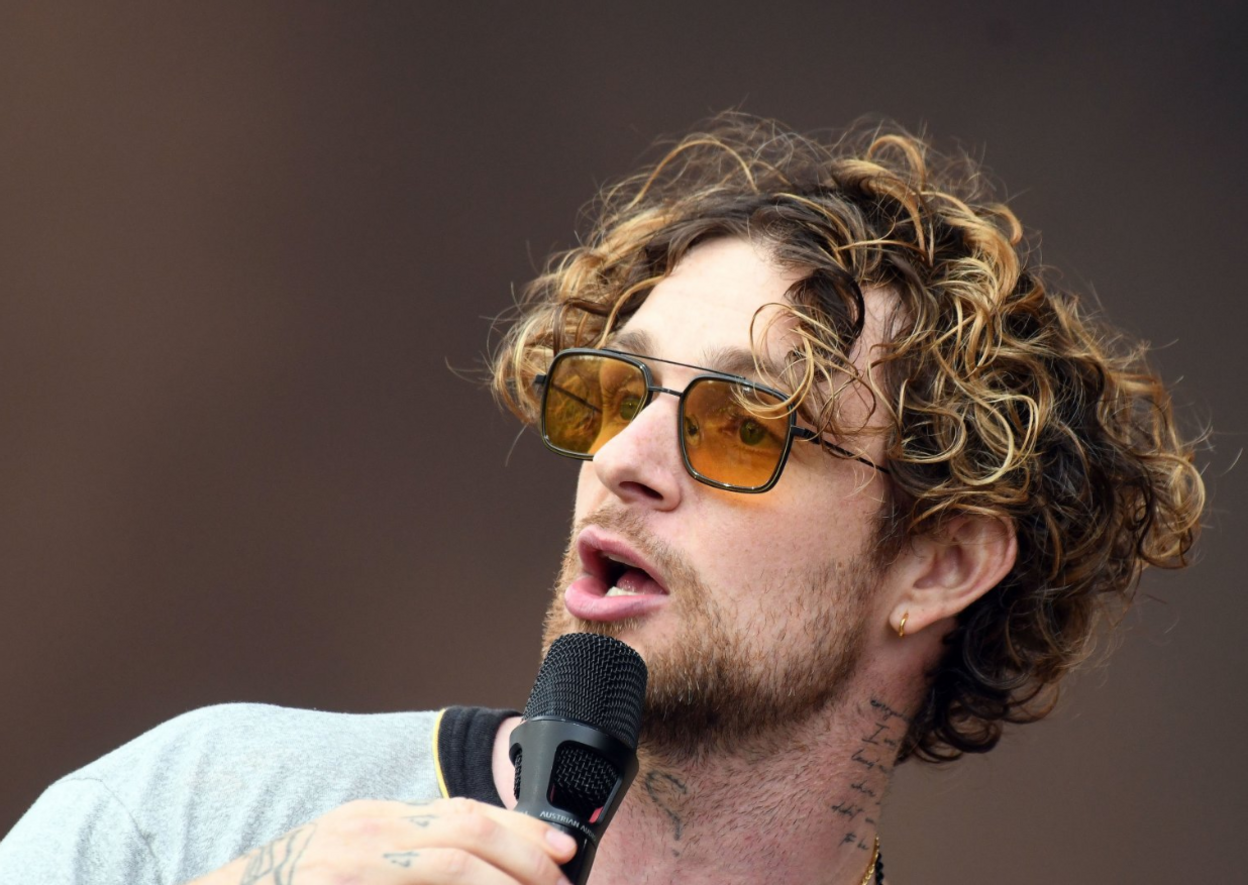 Tom Grennan wearing tinted sunglasses as he sings into a microphone