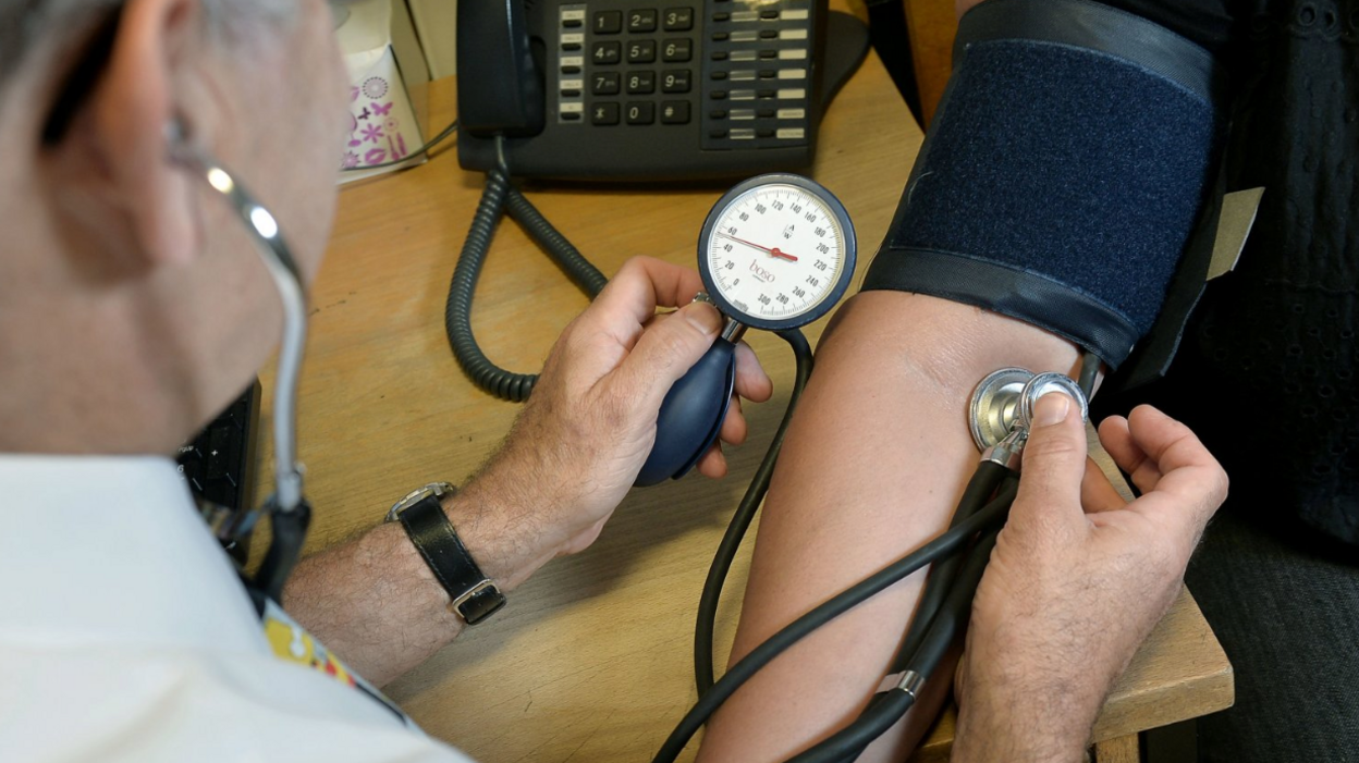 A doctor tests the blood pressure of a person whose arm can be seen.