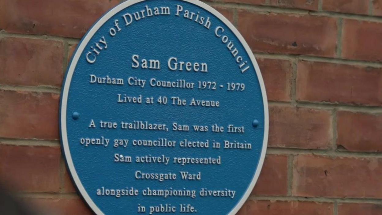 A round blue plaque with white writing saying Sam Green was a Durham County Councillor from 1972 to 1979 and lived at 40 The Avenue. It also says that Green was a true trailblazer and the first openly gay councillor to be elected in Britain and that he represented the Crossgate Ward. 