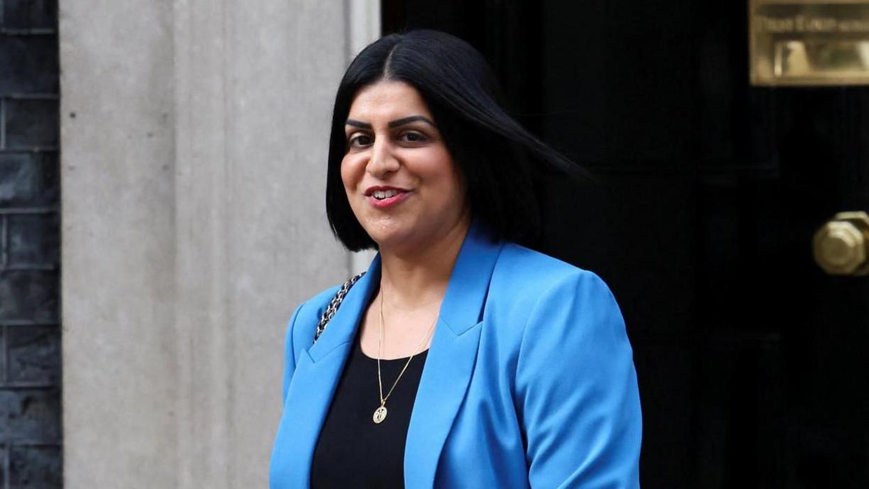 Shabana Mahmood, wearing a turquoise suit, smiles to the camera as she leaves 10 Downing Street.