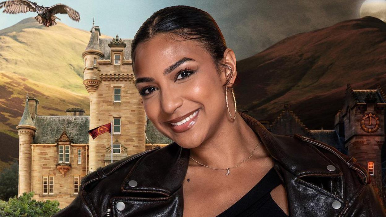 Maia, a 25-year-old woman. Her dark hair is pulled back from her face and neck. She is tilting her head to her right and is smiling broadly. She is wearing large gold hoop earrings and a brown collared black leather jacket. Behind her are hills rising to the sky and a stone Scottish baronial-style castle with creamy stone, a grey slate roof and turrets. An eagle is flying in the sky above the castle