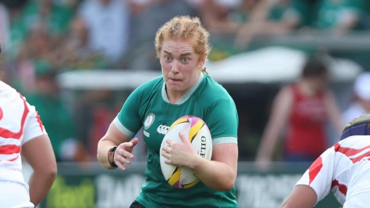 Niamh O'Dowd running between two players with the ball under her left arm during a World Cup match