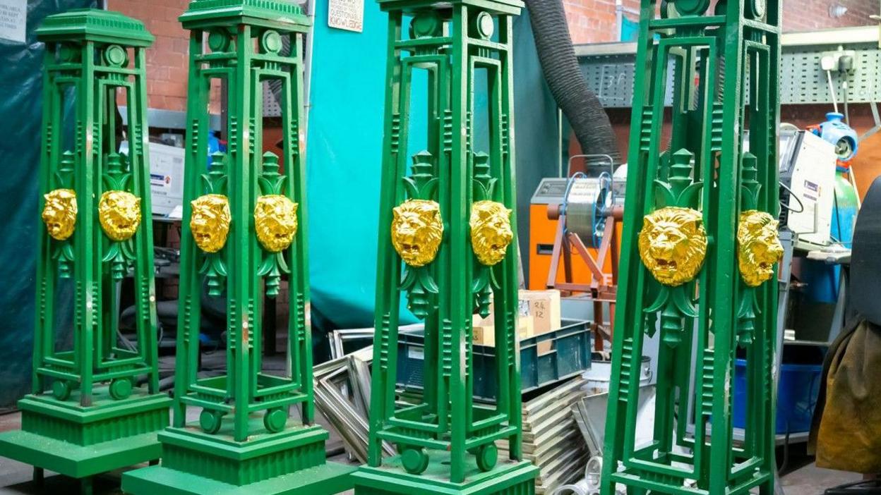 Restored green lighting columns for Queens Park Bridge, Heywood, with gold painted lion heads at the  workshop where they were restored